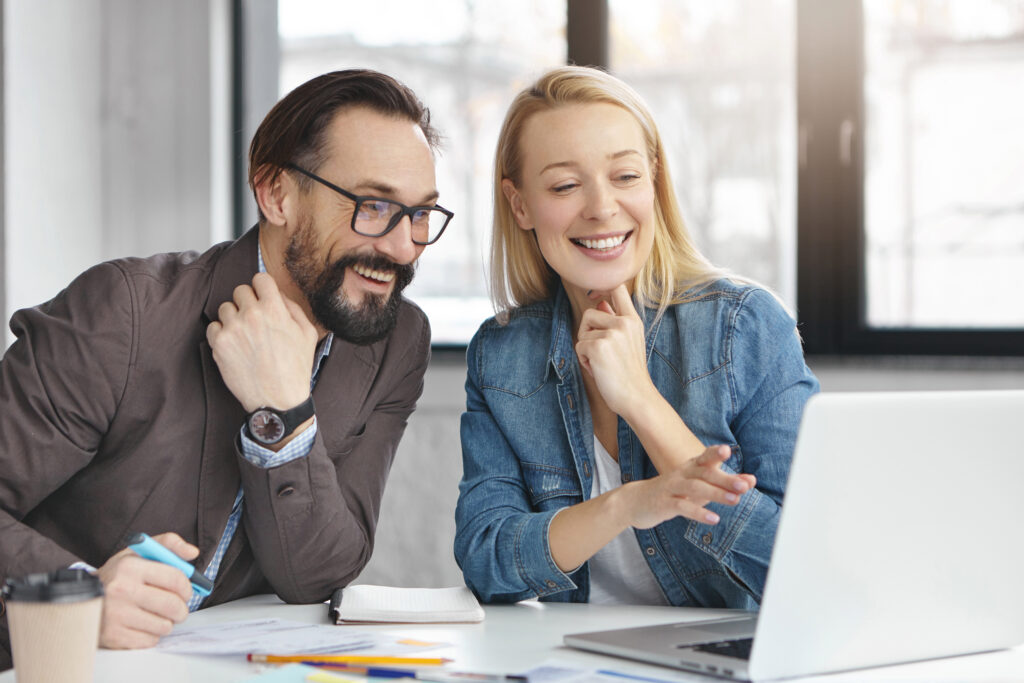 cheerful experienced male and female executive managers of prosperous company discuss details of working process, search needed information on modern laptop computer, use free internet at cabinet